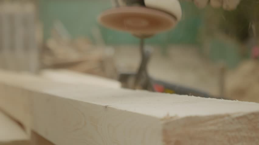 A worker sands down wooden beams with an angle grinder, carefully removing rough edges and preparing the wood for further construction tasks.