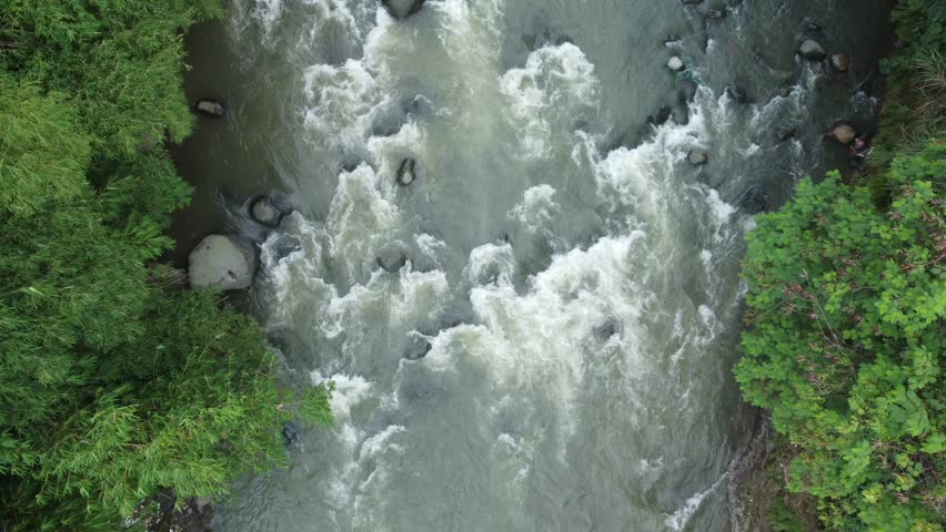 Top-down view of a fast-moving river with rapids surrounded by forest trees. Shot in Indonesia.