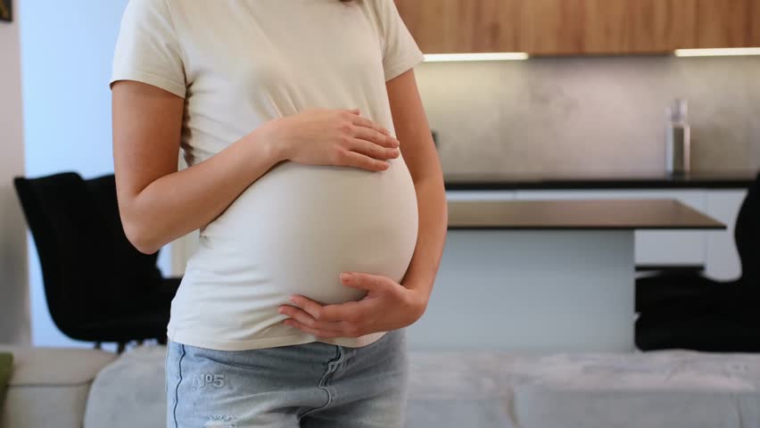 A pregnant woman at home, holding her belly and enjoying a peaceful moment in a modern kitchen
