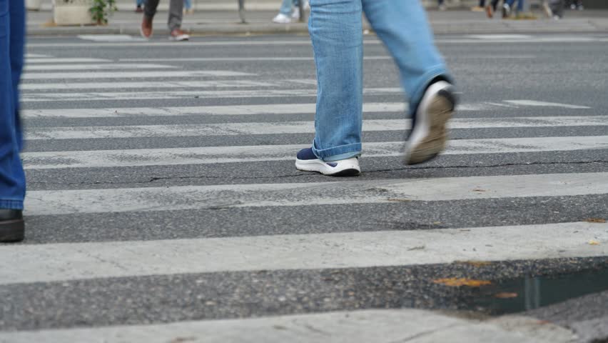 Pedestrians crossing a busy city street on a zebra crosswalk, showing urban life concept, people legs, low angle view
