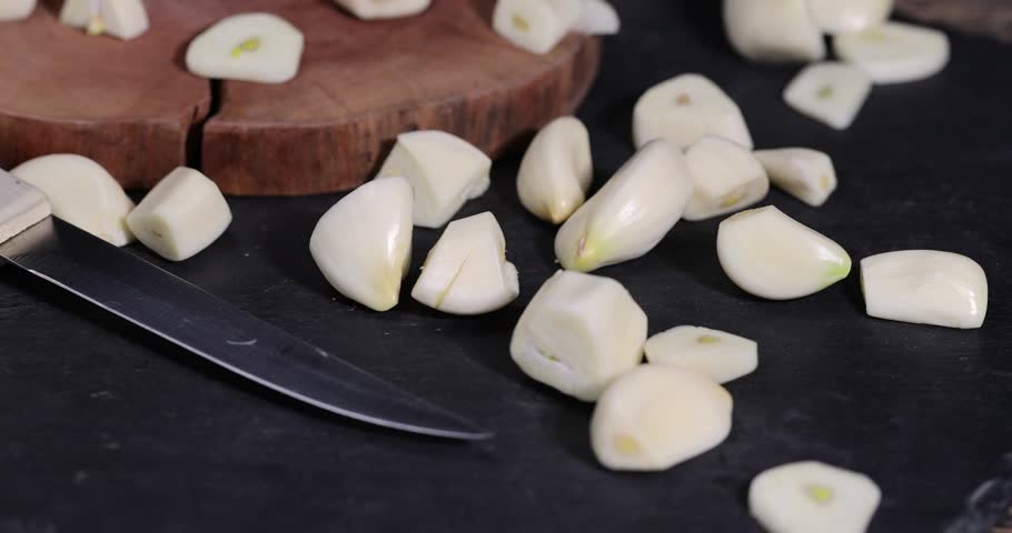 peeled and sliced purple garlic scattered on the black kitchen table and peeled and sliced, fragrant fresh and natural garlic spices