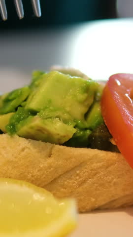 Avocado tomato toast Woman eating toast with avocado and tomatoes sitting at a table in a restaurant