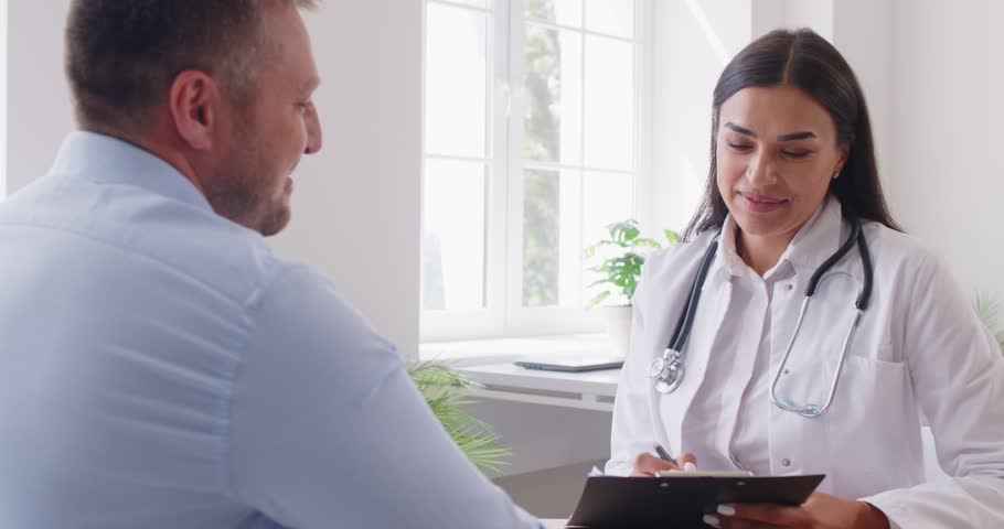 Doctor or nurse performs a medical exam for a man patient during a clinic visit. Healthcare professionals engaging in conversation and providing medical care in a clinical setting.