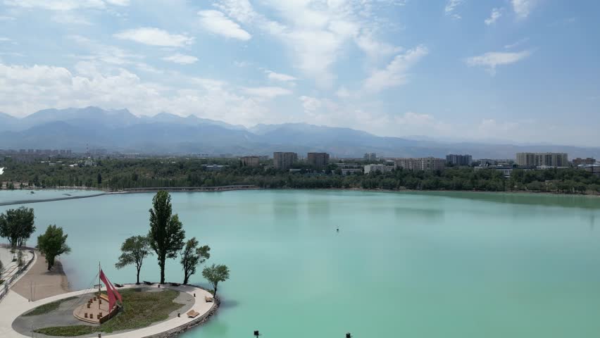 Aerial view of a turquoise lake in the city. Huge mountains in the background.