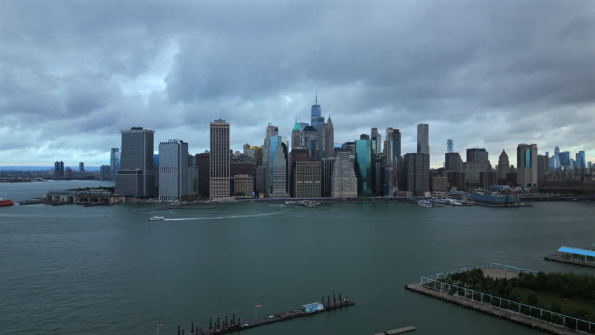 Breathtaking Aerial drone shot of New York City, New York showing tall skyline towers, wide river water and textured clouds forming a dramatic bright city panorama.