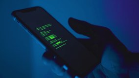 Hand holding smart phone on dark blue background while malware app is installed. Close up on device hacking code running on screen downloading and setup of illegal criminal spyware cybersecurity virus - Powered by Shutterstock - Get 15% off with code: PIKWIZARD15