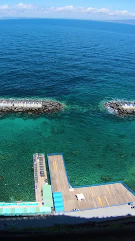 Aerial views of the coastline and seaside bathing platforms overlooking the clear waters of the Mediterranean Sea. Documentary footage showing coastal landscape, cliffs and summer tourism in southern Italy.