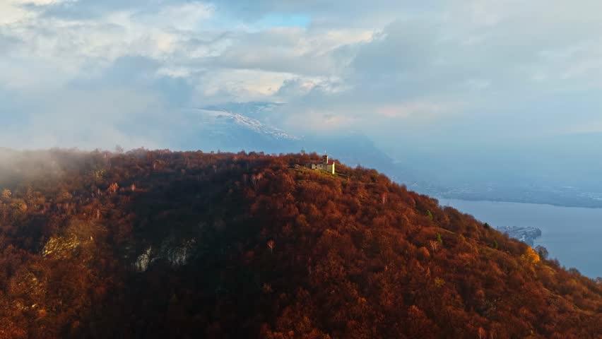 Aerial approach of autumn colored hillsides and forest overlooking Lake d’Iseo in northern Italy, castle overlooking the coast