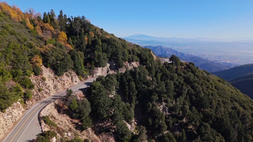 High aerial flyover of stunning landscapes along the winding Rim of the World Scenic Byway in the San Bernardino National Forest with clear sky