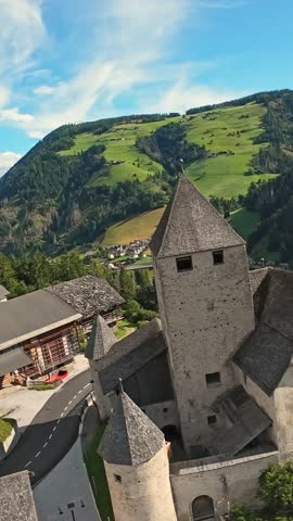 Vertical Screen Aerial Tower Above Green Alpine Slopes, Sunlit Turrets And Village Rooftops, Sweeping Meadow And Mountain Ridgelines, Dramatic Sky With Cirrus Clouds, Travel And Hiking