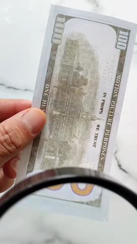 Counterfeit money. A man examines a hundred-dollar bill with a magnifying glass. Looking for watermarks on the bill. The concept of counterfeit money exchange.