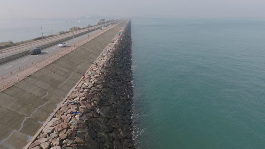 People fishing on the seawall roadway bank and fast-moving vehicles 4k