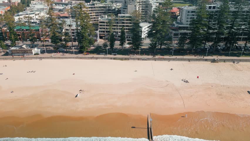 Cinematic 4K drone footage of Manly Beach on a hot summer’s day, featuring surfers riding waves, tourists enjoying the shoreline, and vibrant blue ocean water along Sydney’s iconic Northern Beaches.