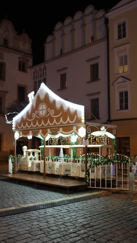 Vertical screen illuminated christmas train ride on historic city square with festive lights and empty wagons at night during winter holidays