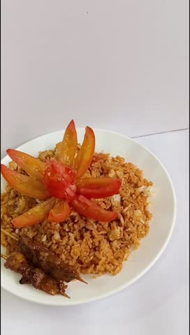 Indonesian Fried Rice (Nasi Goreng) with Chicken Satay Skewers and Tomato Garnish on White Plate — Close-Up Food Video