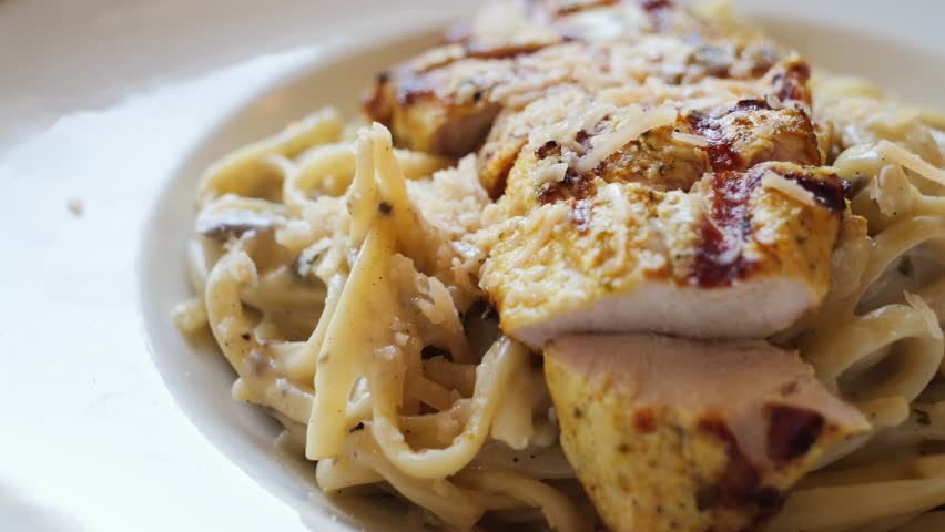 Creamy carbonara pasta with chicken breast, mushrooms, and parmesan cheese. Close up of takes pasta with a fork. High quality 4k footage