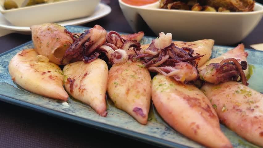 Baby squid in basil sauce with lemon sprinkles on a plate at a snack bar. High quality 4k footage