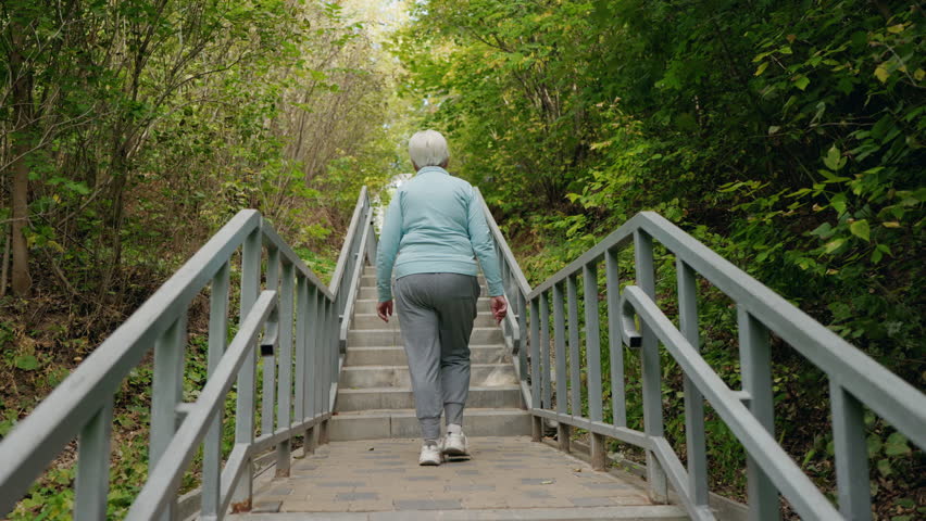Elderly woman confidently walking up outdoor stairs in a green park. High quality 4k footage
