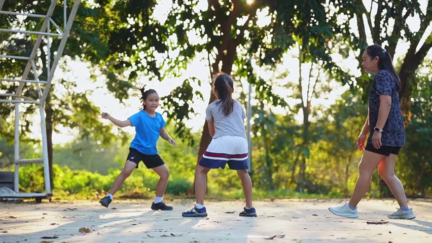 Happy Asian family playing basketball together on outdoor court at the park during golden hour.