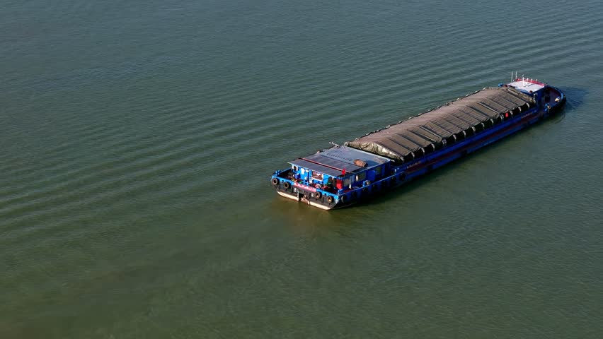 Barge travels on the river at daytime in China, carrying cargo under cover