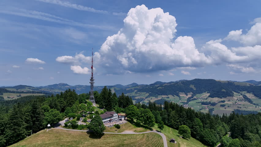 Scenic aerial drone footage of the Bachtel Tower in the Zurich Oberland, Switzerland. Summer landscape with blue sky, mountains and panoramic views