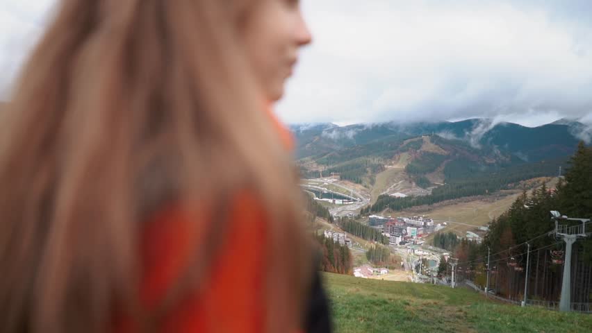 A beautiful young European woman strolls outdoors high in the mountains with an incredible view. A mountain walk and hike on the weekend for relaxation and recharge. Nature and flowers in a field