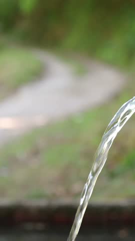 Close up of a person filling a stainless steel canteen with fresh water from a fountain. A blurred hiking trail is visible in the background