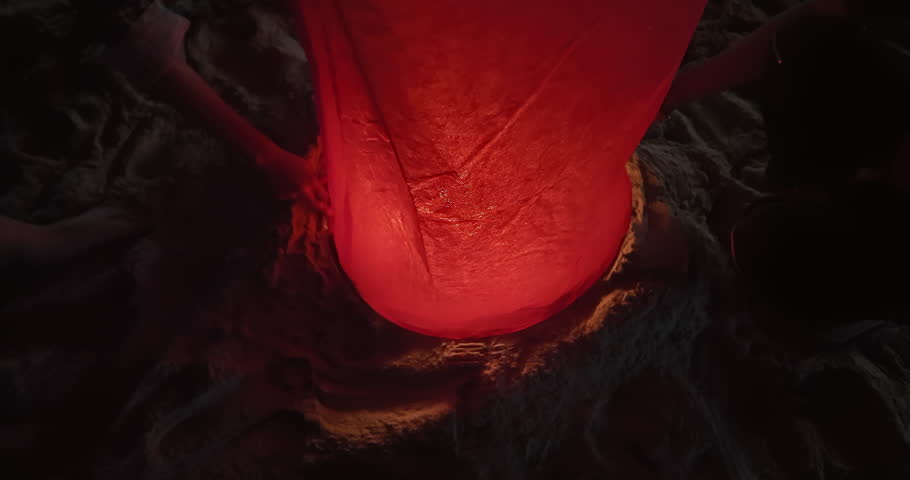 close up of a person holding a glowing red sky lantern at night on the beach.