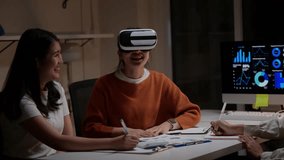 Young Asian businesswomen in a late-night meeting. One colleague wearing a VR headset interacts with a virtual interface for data visualization - Powered by Shutterstock - Get 15% off with code: PIKWIZARD15
