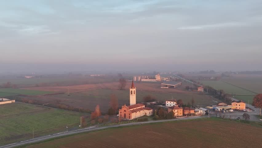 Rural Italian countryside showing Strada Padana Inferior S.S.10 Via Mantova road with passing cars, near iconic Trattoria La Resca restaurant and San Bartolomeo church in Vescovato, Cremona, Italy