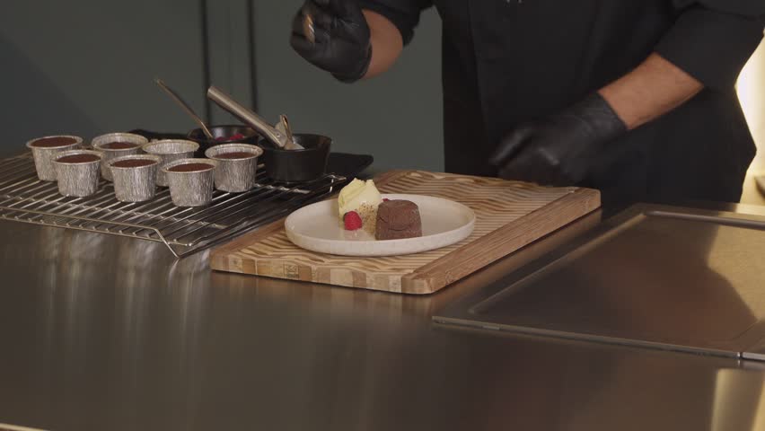 Gloved chef plating chocolate lava cake with ice cream in kitchen
