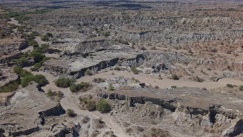 Cinematic drone footage glides above the grey desert of Tatacoa, Colombia, showcasing dramatic erosion, winding canyons, and the vast, otherworldly landscape shaped by time and arid climate textures.
