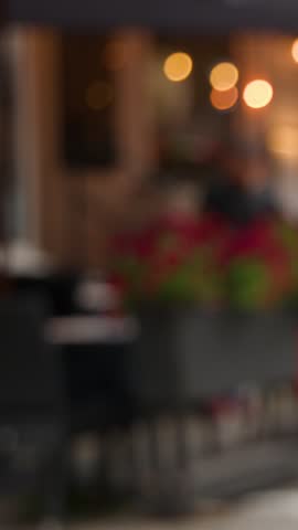 Out-of-focus people walk by illuminated street cafÃ©, evening urban scene, soft bokeh lighting