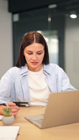 Smiling woman completes an online purchase using credit card on laptop. Displays happiness and satisfaction after successful transaction, celebrating modern digital shopping experience with pure joy.