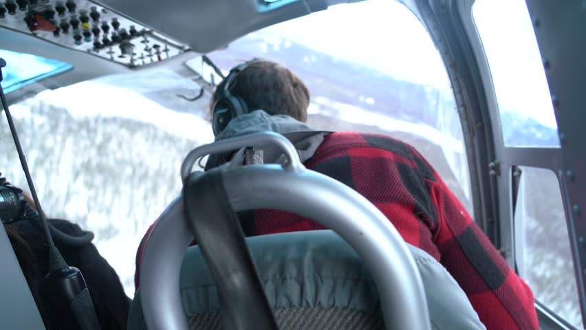 Aerial view from inside helicopter cockpit during scenic winter flight near Whitehorse, Yukon Territory, Canada. Remote wilderness view with snow-covered boreal forest and mountains