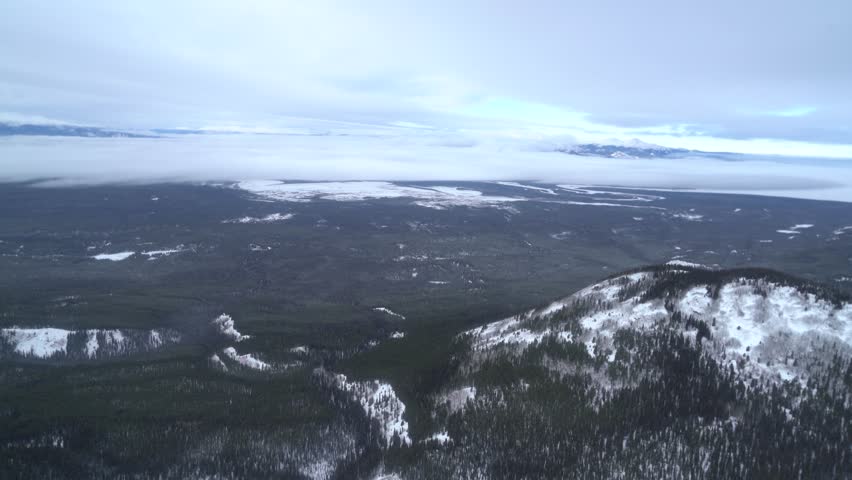 An aerial tracking shot from a helicopter over expansive, snow-covered boreal forests and mountains near Whitehorse, Yukon, Canada, capturing a vast, rugged winter landscape