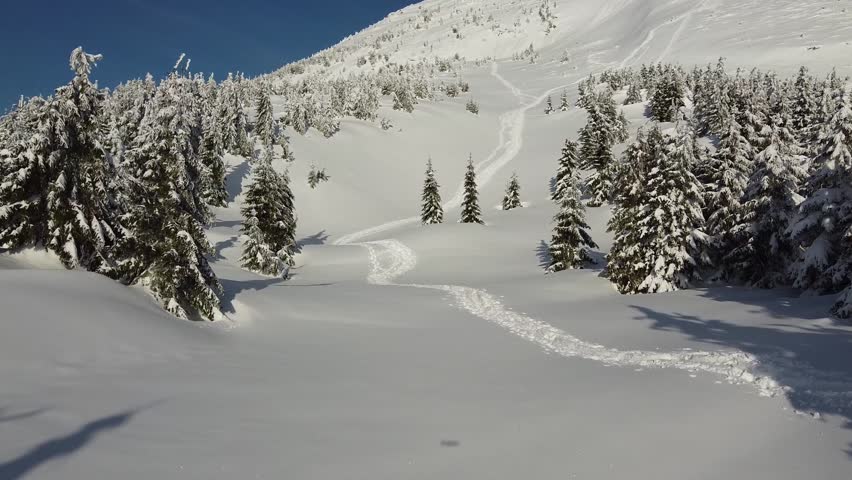 Aerial drone footage of a winter mountain landscape with a winding footpath and footprints in fresh snow.