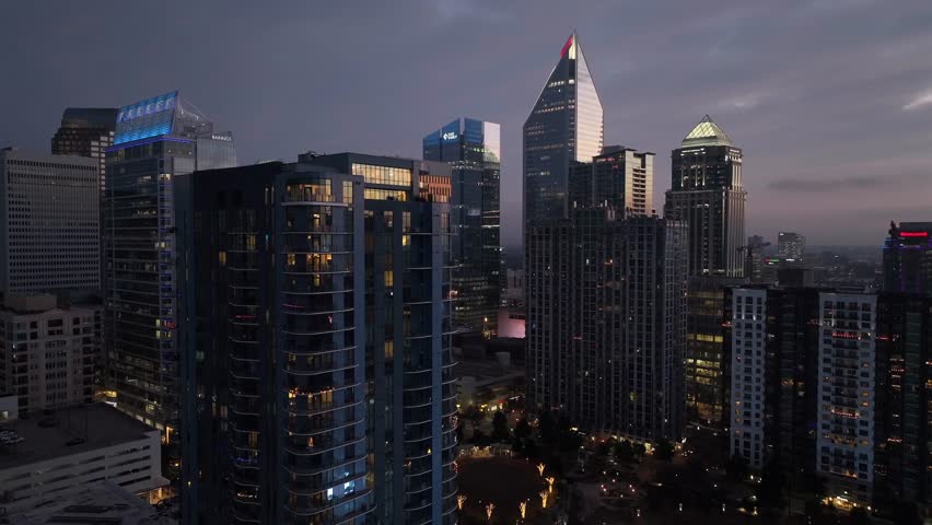 Aerial view of Charlotte skyline at dusk, with illuminated modern skyscrapers rising above city as evening light fades, showing vibrant financial district and contemporary urban atmosphere.Rising shot