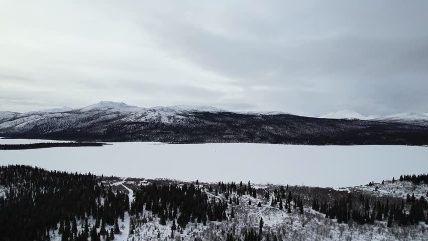 An aerial view captures the vast, snow-covered landscape and frozen surface of Fish Lake (Łu Zil Män), located near Whitehorse, Yukon, Canada. This area, significant to the Kwanlin Dün First Nation, is a popular winter destination for outdoor activities and viewing the Northern Lights