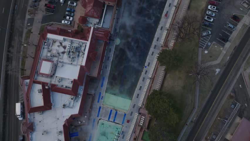 Aerial drone footage starting over the hot springs and tilting up to reveal Glenwood Springs Colorado, surrounded by the Colorado Rocky Mountains in clear daylight.