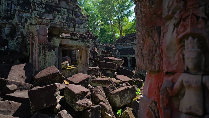 Walking through Preah Khan Temple ruins as the camera pans left past collapsed stone blocks and doorways in Siem Reap