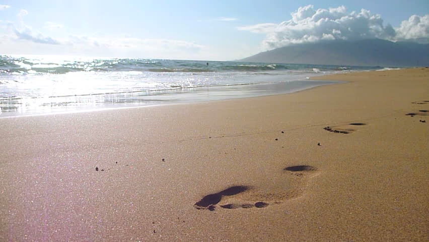 Waves crashing on shore wipe away footprint in the sand on beach in Hawaii.
