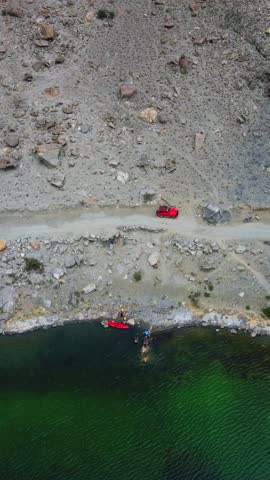 Aerial view of the stunning green waters of Borith Lake contrasting with the rocky terrain and red vehicles, Borith Lake, Gilgit Baltistan, Pakistan.