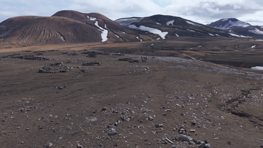 Aerial view of hikers trekking through the rugged, snow-dusted volcanic highlands of Landmannalaugar, Iceland.