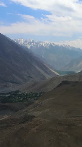 Aerial view of the glacier contrasting with the snow-capped mountains and the village nestled between the valley, Passu Glacier, Gilgit Baltistan, Pakistan.