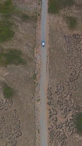 Aerial view of a lone vehicle making its way down a long road, surrounded by barren land in the park, Deosai National Park, Gilgit Baltistan, Pakistan.