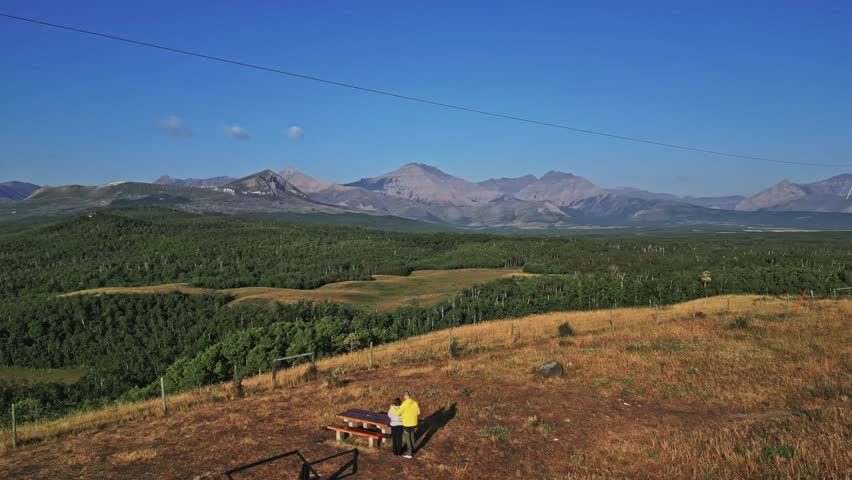 Aerial view of lush green trees meets majestic mountains under clear blue sky, creating a stunning contrast of colors, Twin Butte, Alberta, Canada.