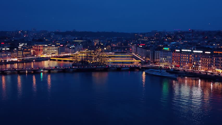 Aerial view of the illuminated Pont du Mont-Blanc reflecting off the dark waters, contrasting with the city lights, Geneve, Geneve, Switzerland.