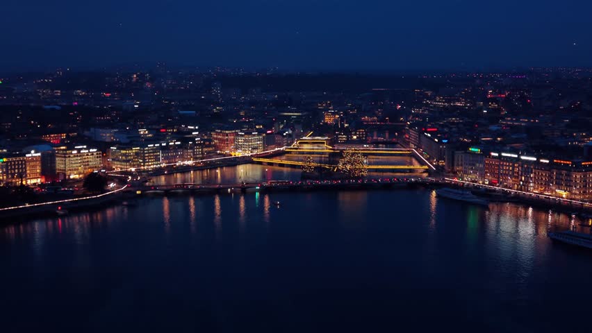 Aerial view of the brightly lit Pont du Mont-Blanc bridge reflecting on the dark water, contrasting with the city lights, Geneve, Geneve, Switzerland.