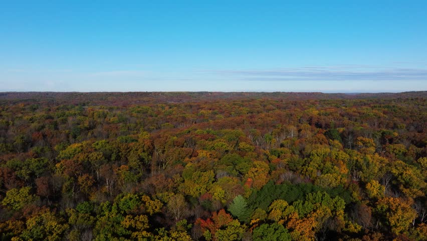 Broad aerial pullback of Brown County fall forest extending across rolling hills and open horizon, Indiana USA